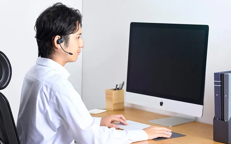 男性がヘッドセットを装着し、パソコンに向かって作業している様子。